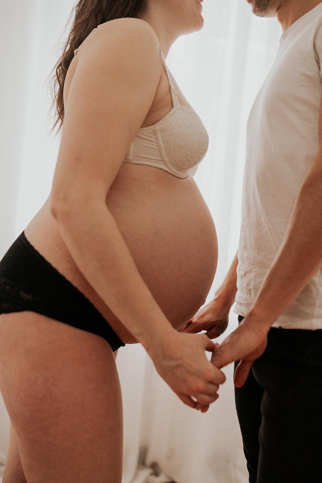 Babybauch im Profil, die Hände der werdenden Eltern liegen darunter
