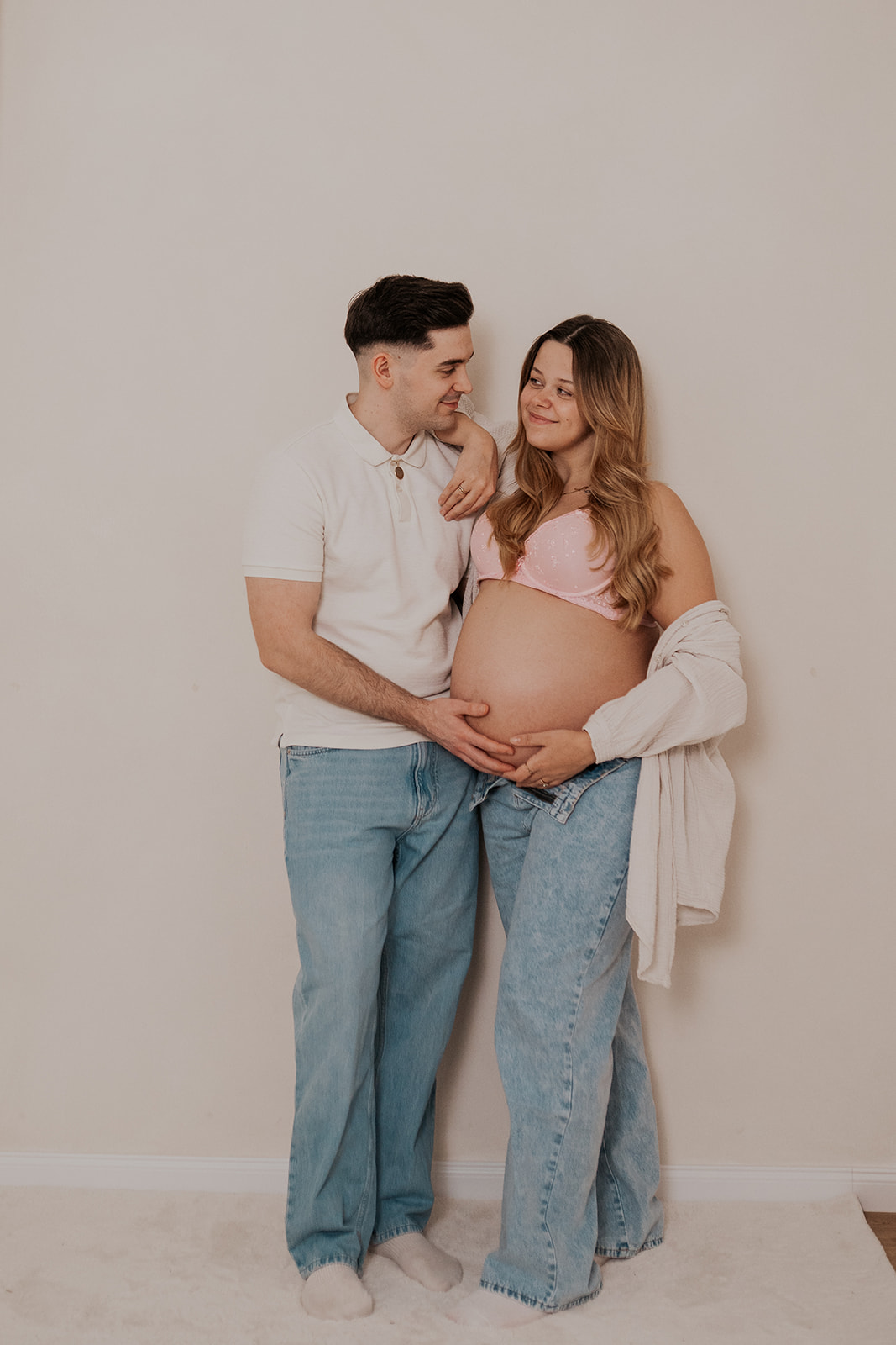 Werdende Eltern im hellen Studio, beide Hände am Babybauch