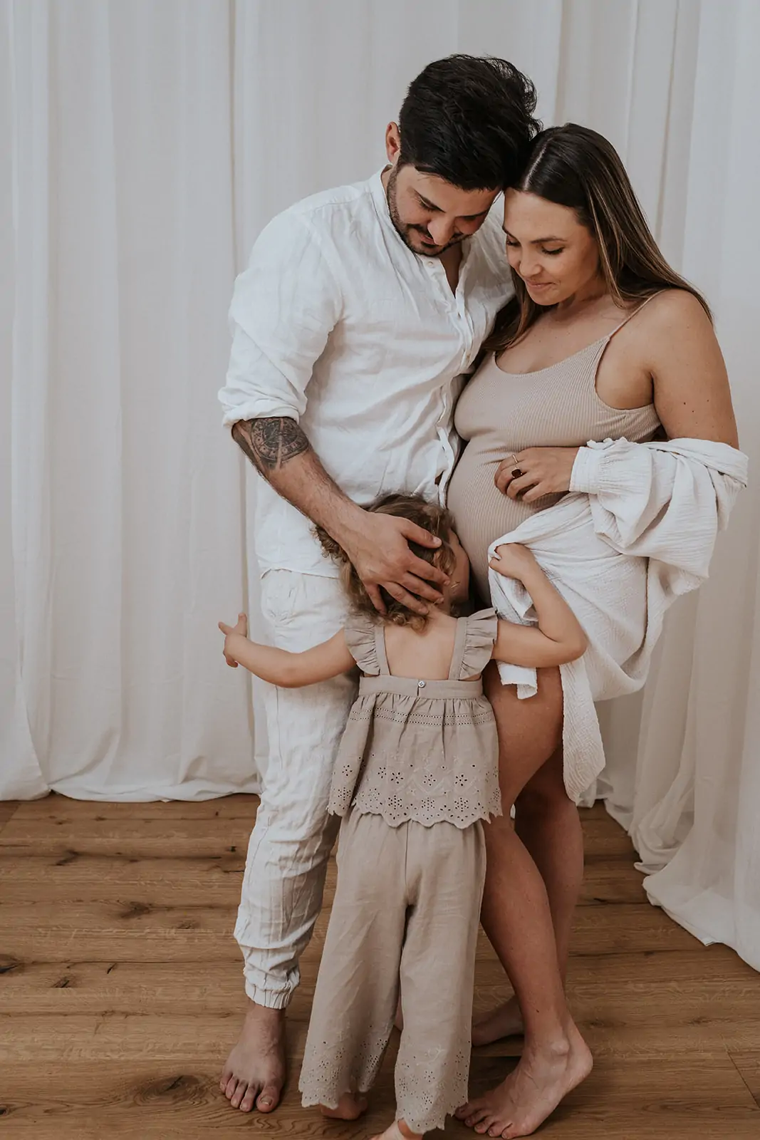 Familie mit ihrer kleinen Tochter, alle drei am Babybauch