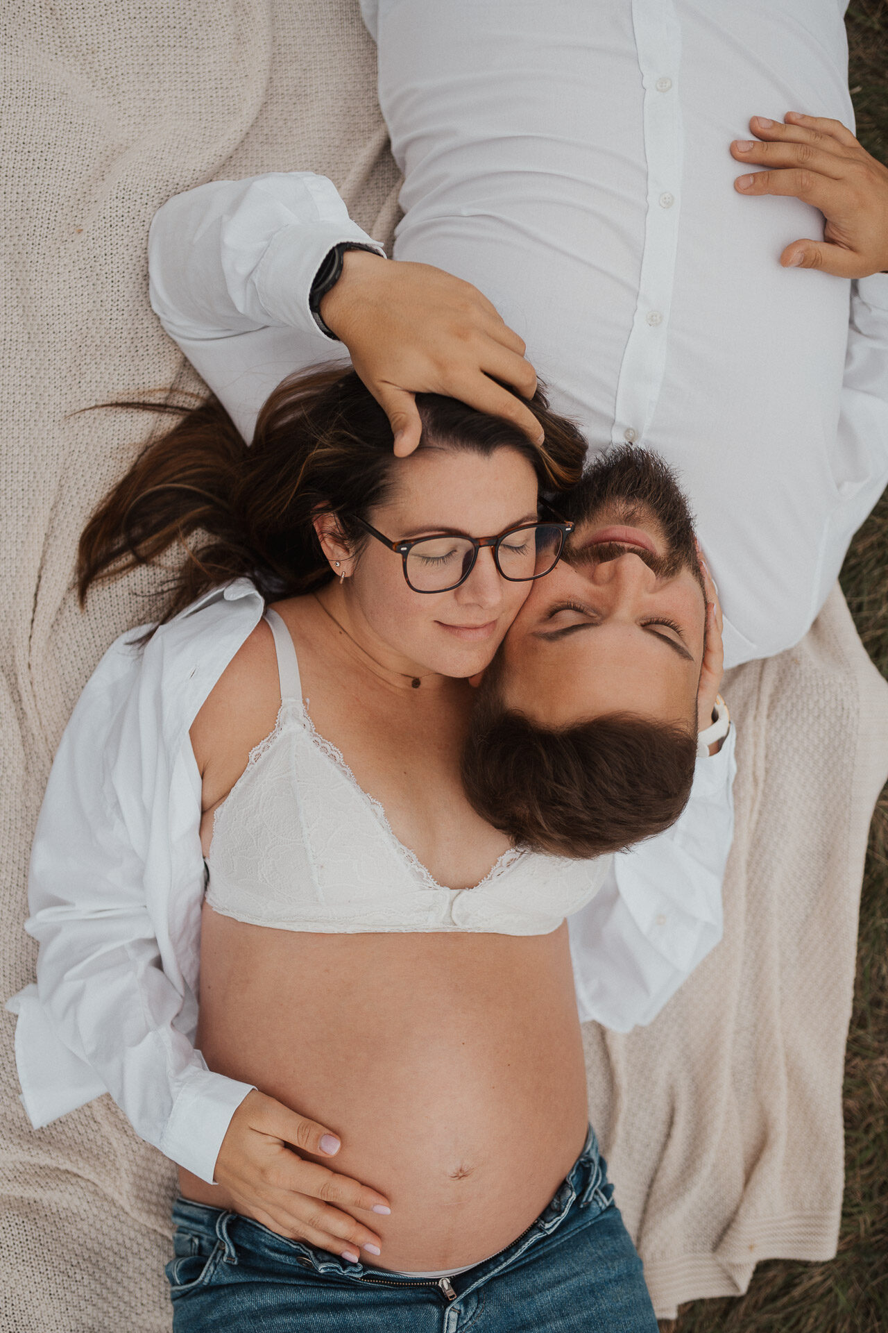Schwangere liegt entspannt da, ihr Partner schmiegt sich an den Babybauch