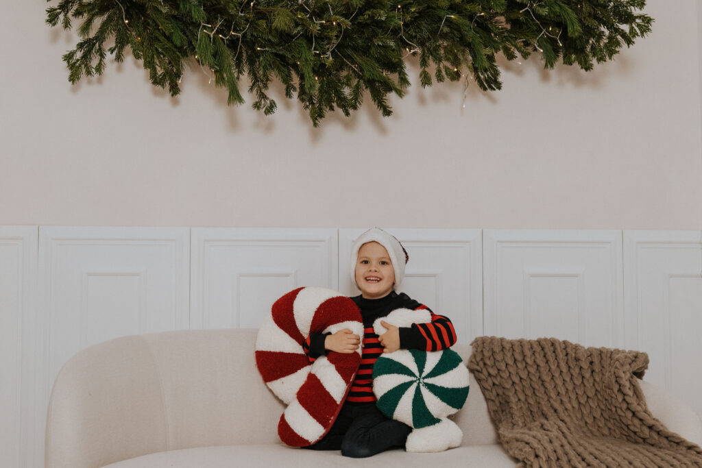 Lachendes Kind mit Weihnachts-Kissen auf dem Sofa im weihnachtlich dekorierten Studio